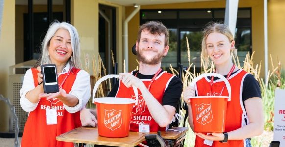 Three Salvos Red Shield Appeal volunteers with donation buckets and Eftpos